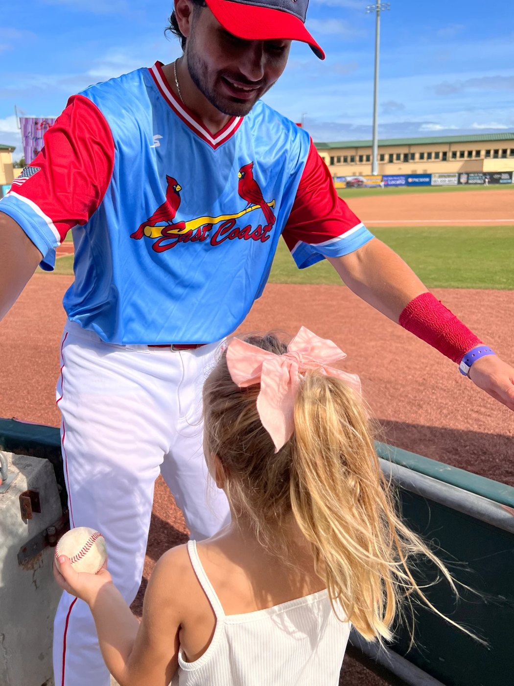 A ballplayer leaning over the rail to hand a baseball to a young girl at the fence